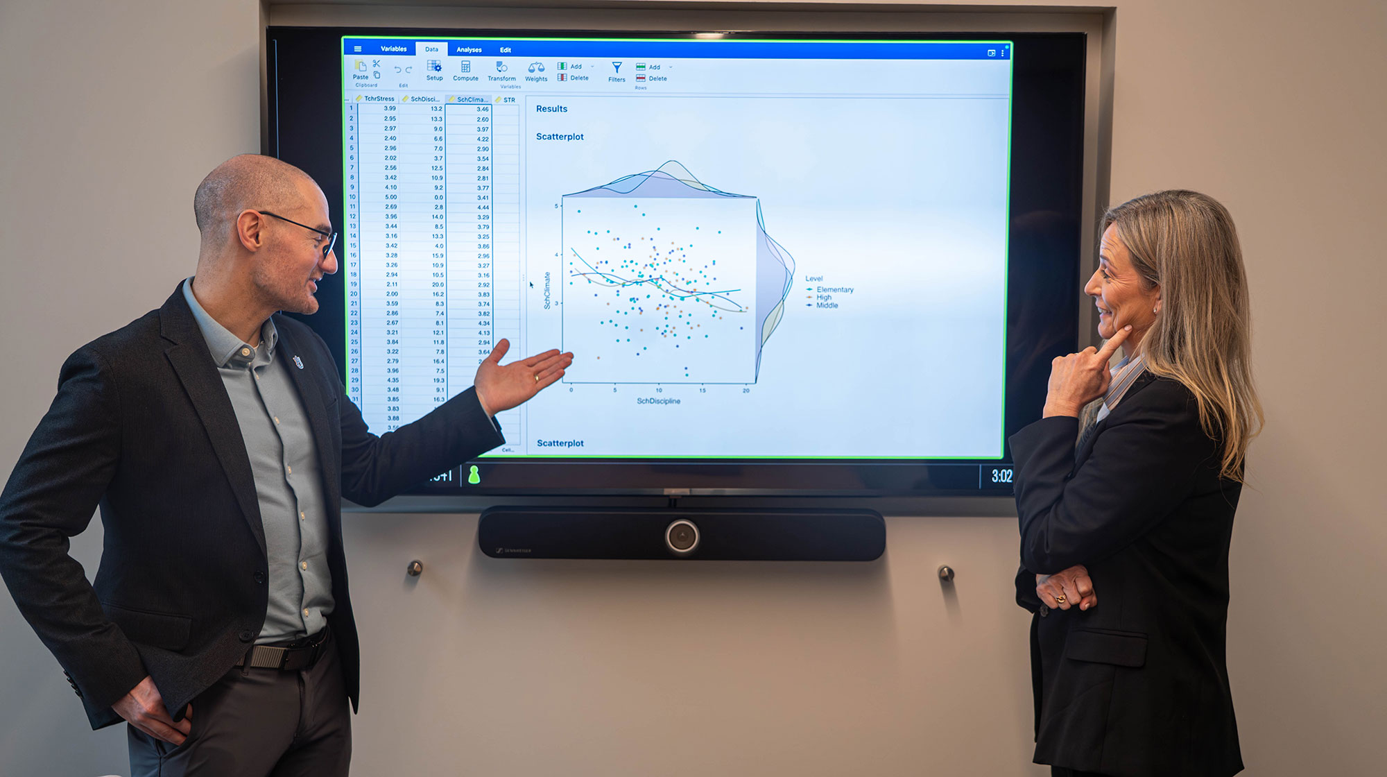 A faculty member and a graduate student discuss a presentation on the board behind them.
