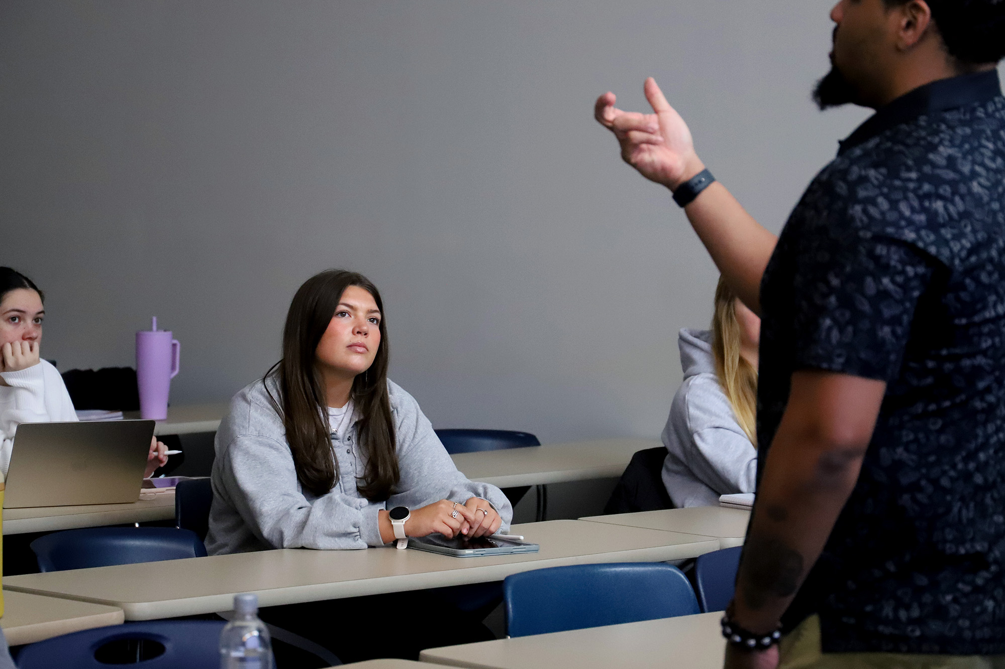A teacher speaks to students at tables in a classroom