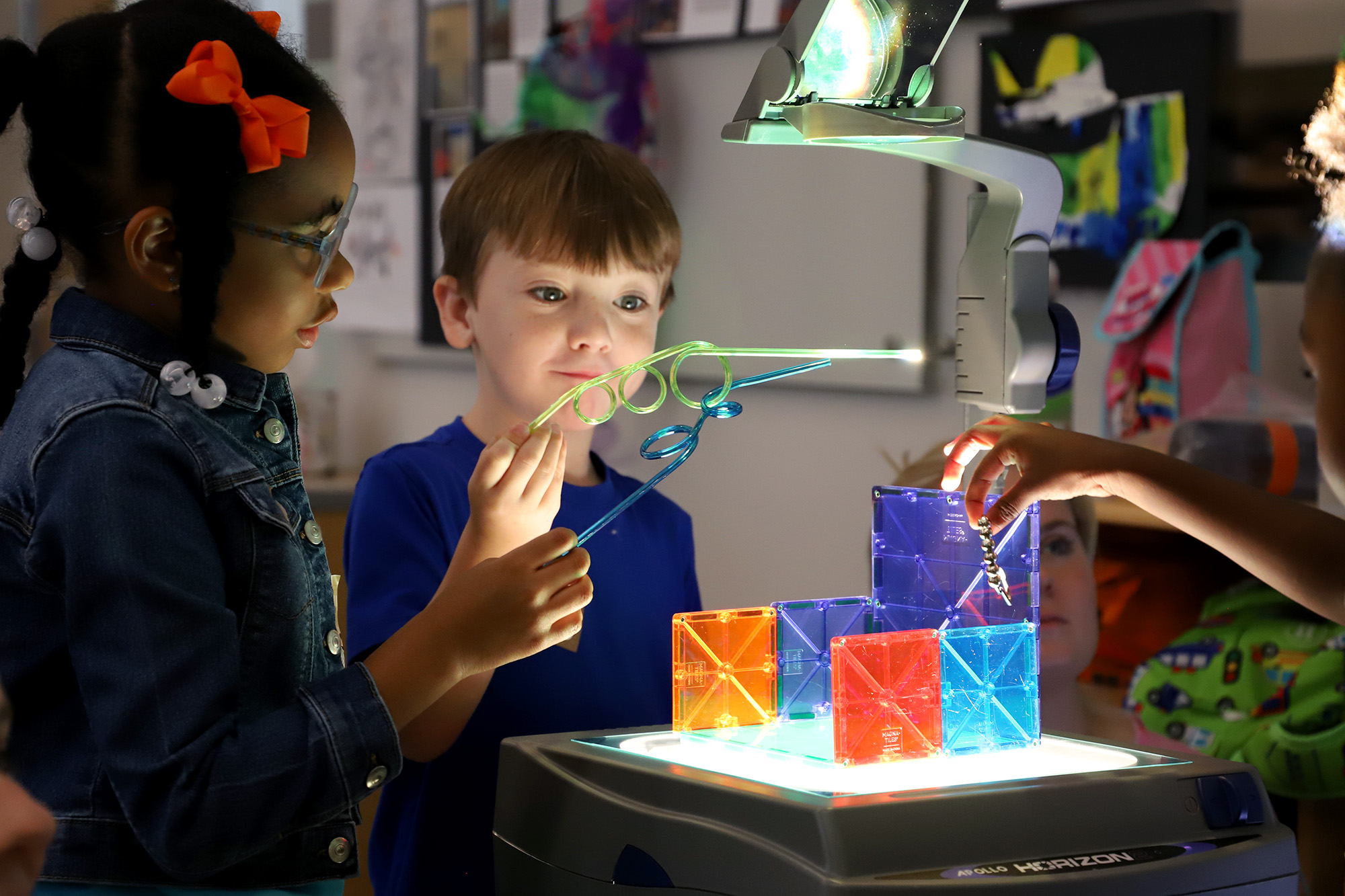 A young boy and girl play with twisty straws and colored tiles.