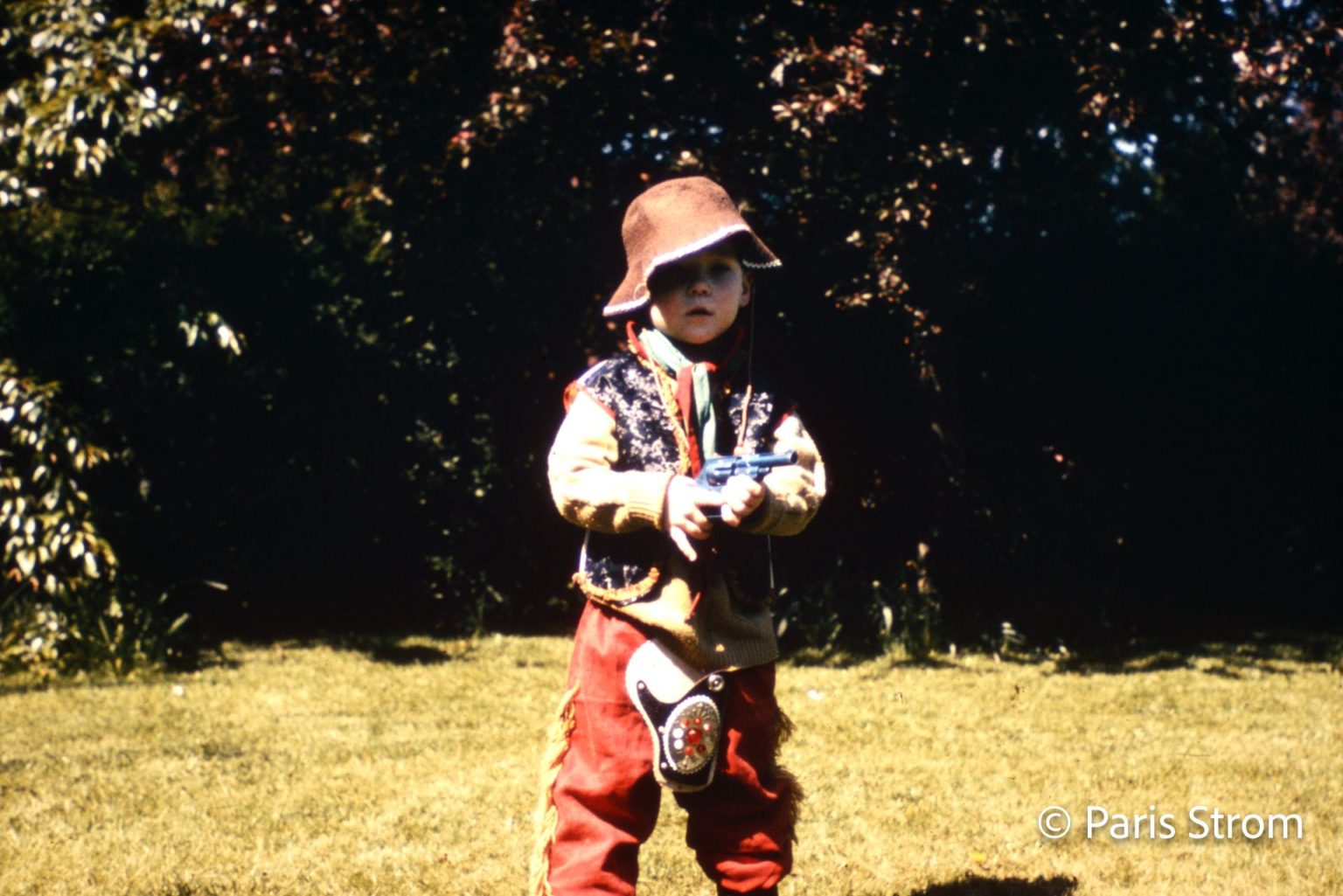 A young boy is dressed as a cowboy and holding a toy gun
