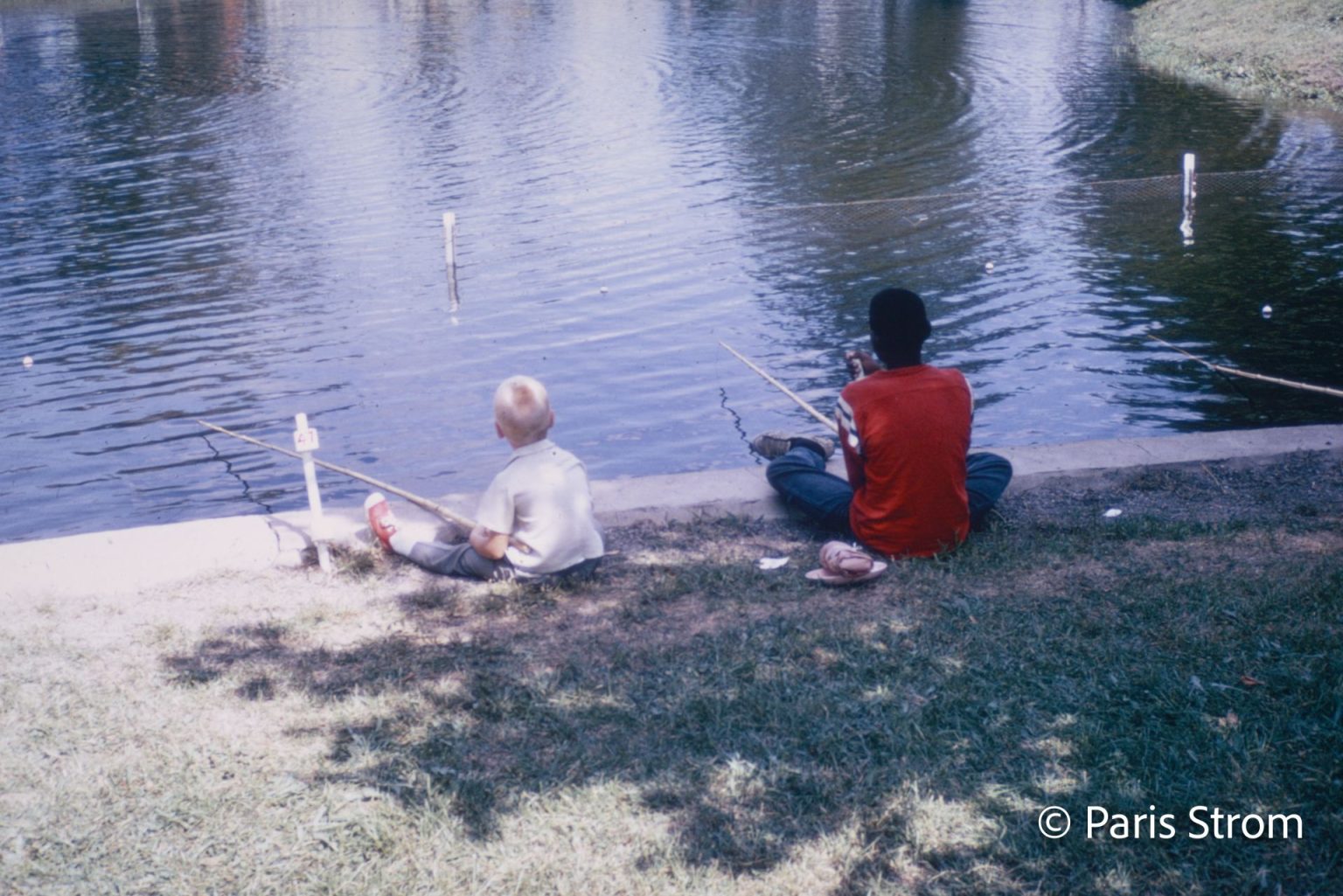 Two young boys hold fishing poles over a pond.