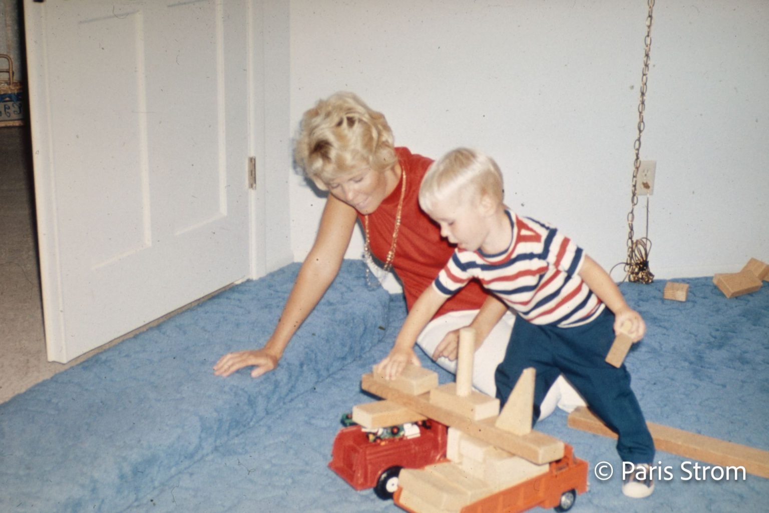 A young boy and his mother play on the floor with blocks and toy trucks.