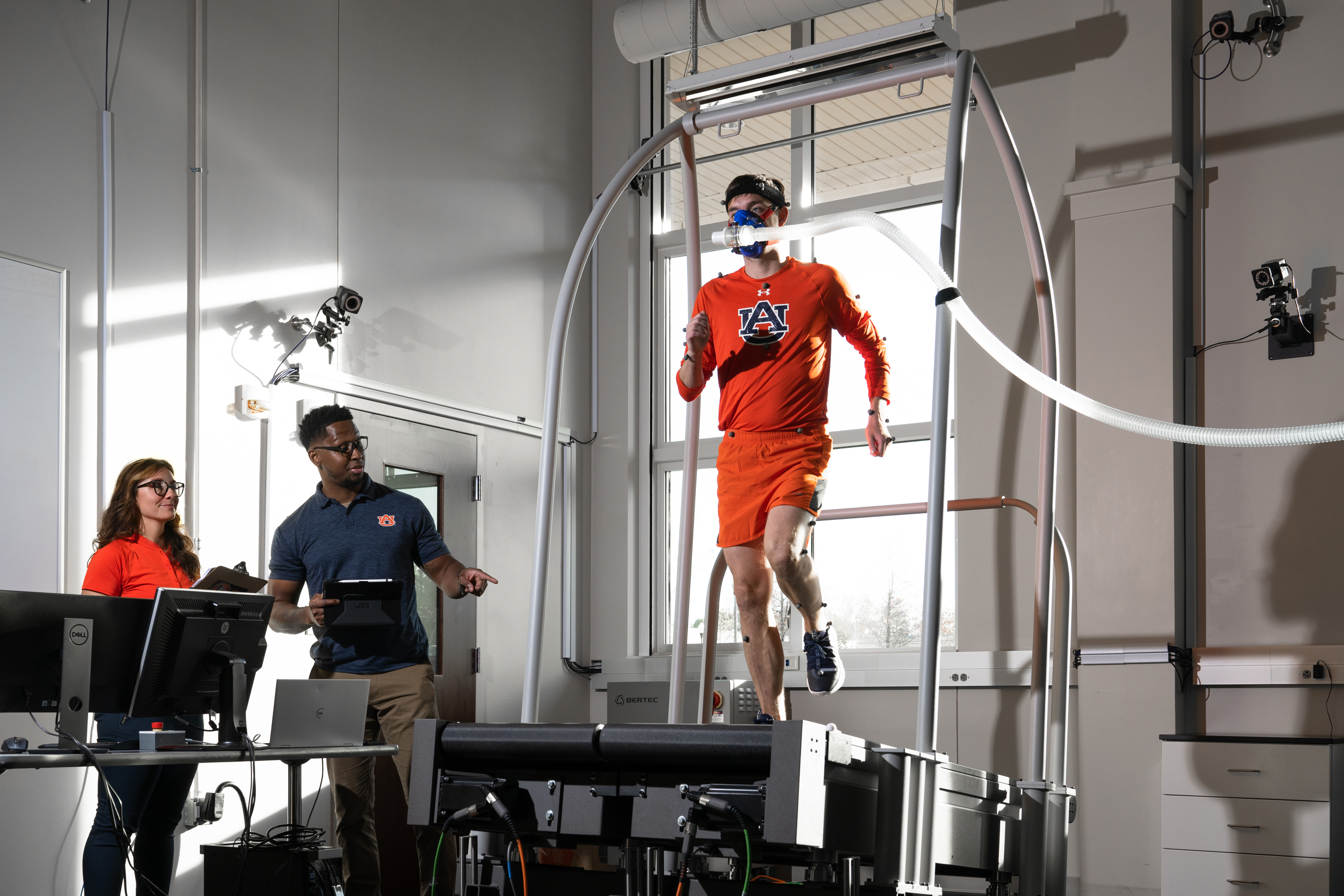 A research participant walks on a split treadmill while two researchers watch and collect data.